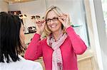 Happy senior woman trying on glasses in store