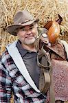 Portrait of a happy mature cowboy carrying saddle