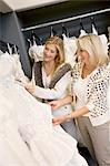 Cheerful young daughter with senior mother selecting wedding dress in bridal boutique