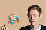 Mid adult man looking at lollipop over colored background