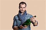 Portrait of a confident young man with champagne bottle over colored background