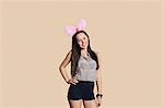 Portrait of a beautiful young woman wearing bunny ears with hands on hips over colored background