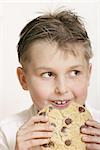 Boy with a very large choc chip cookie!!  A few crumbs on his face.