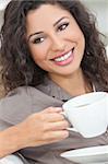 Beautiful young Latina Hispanic woman smiling, relaxing and drinking a cup of coffee or tea