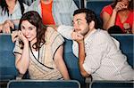 Embarressed young woman with flirting boyfriend in theater