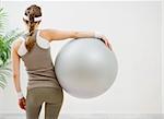 Athletic woman with fitness ball standing back to camera