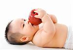 Pan Asian baby boy eating red apple on bed