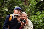 Two seniors with camera and binoculars in forest