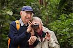 Senior man helps wife look through binoculars in forest