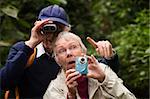 Man helps senior lady use camera in a forest