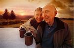 Happy senior couple drinking coffee outside during sunset