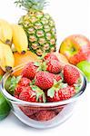 Arrangement of various fresh ripe fruits: pineapple, bananas, oranges, apple, limes and strawberries in a glass bowl closeup isolated on white background.