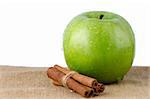 Ripe green apple with cinnamon sticks over rafia on white background