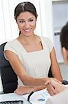 Beautiful young Latina Hispanic woman or businesswoman sitting at a desk in an office meeting shaking hands