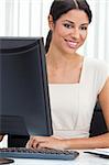 Beautiful young Latina Hispanic woman or businesswoman in smart business suit sitting at a desk in an office using a computer