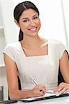 Beautiful young Latina Hispanic woman or businesswoman in smart business suit sitting at a desk in an office writing