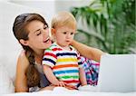 Mother showing something to baby on laptop
