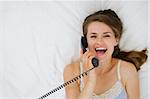 Portrait of woman laying on bed and speaking phone. Upper view