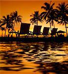 Row deckchairs with water reflection on beach at sunset, Tanjung Aru, Malaysia.