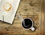 Cup of hot black coffee on rough wooden table with stain rings