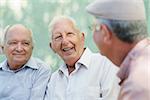Active retirement, group of three old male friends talking and laughing on bench in public park