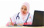 Muslim female doctor writing report on her working desk