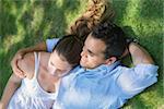 Happy beautiful young man and woman in love, lying on grass in park and relaxing