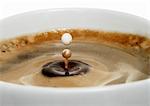 A drop of milk falling into a cup of coffee (close-up)