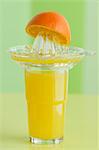 A glass of orange juice, a juicer and an orange half