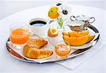 Le petit déjeuner avec jus de melon, croissants, oeufs, confiture, café et orange