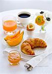 Le petit déjeuner avec jus de melon, croissants, oeufs, confiture, café et orange