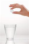 A hand holding an effervescent tablet over a glass