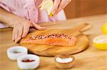 Woman Squeezing a Lemon Wedge over Salmon