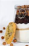 A hazelnut biscuit next to a jar of ingredients