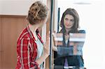 Two female friends looking at each other through a glass door