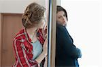 Two female friends standing back to back against a door