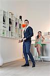 Man cleaning a bookshelf with his wife drinking champagne in the background