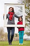 Femme et son fils tenant un cadre photo dans un parc