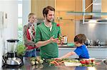 Die Eltern an ihren Sohn schneiden Gemüse in der Küche