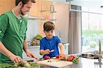 Man looking at his son cutting vegetables in the kitchen