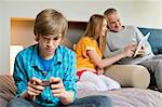 Teenage boy using mobile phone with his father and sister using digital tablet in background