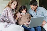 Garçon avec ses parents à la maison à l'aide d'un ordinateur portable