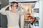 Porträt einer älteren Frau schockiert vor einem Kühlschrank suchen