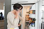 Elderly woman looking at a refrigerator and talking on a mobile phone