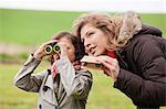 Boy looking through binoculars standing with his mother
