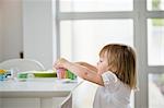 Cute little girl picking up toy tea set from a dining table