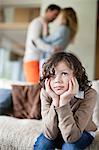 Boy sitting on a couch with his parents romancing in the background