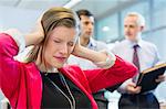 Female executive looking frustrated in an office with her colleagues discussing in the background