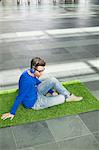 Businessman relaxing on grass and listening to music in an office lobby