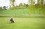 Mann sitzt auf einer Bank in einem Feld